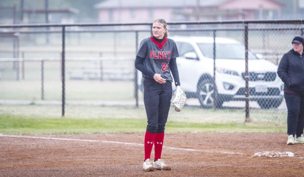OHS Lady Cub #20 Natalie Simmons shivers during the opening innings as drizzle and cold wind blew across the OISD softball field. The weather later broke ever so slightly with the drizzle ending and the wind calming a bit in later innings. Photo by Will S