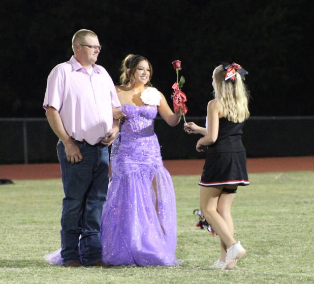 Homecoming Queen nominee Aubree Englishbee with her father, Jake Englishbee, receive a rose from cheerleader Emerald Edgington. Photo by Gina Keating