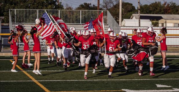 The Olney High School Cubs charge onto the field in Cisco, showing team and patriotic pride in a matchup against the Reagan County Owls. The Cubs fell to the Owls in a game that allowed new OISD Athletic Director and Head Coach Dustin Altmiller to test ne