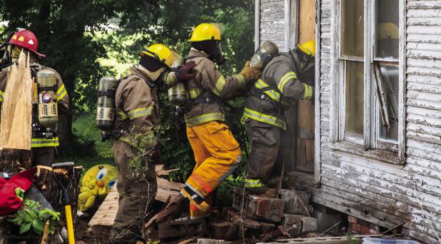A team of Olney and Megargel Volunteer Firefighters breach the smoke-filled house. Firefighters were greeted with choking smoke and visibility reduced to one foot in some parts of the structure. The firefighters’ ability to use oxygen masks and fire-res