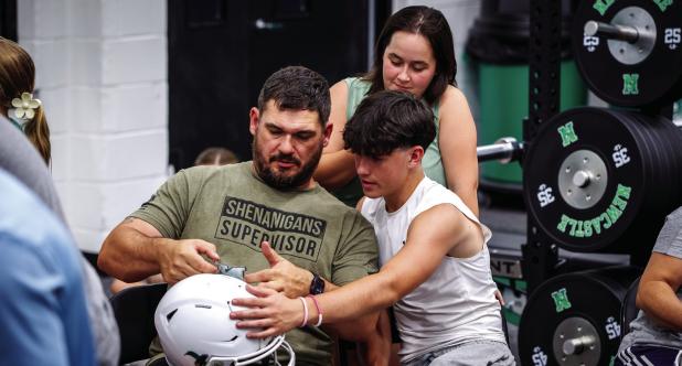 A Bobcat and his dad affix decals on the player’s helmet during the Decals with Dads event. Photo by Will Sadler