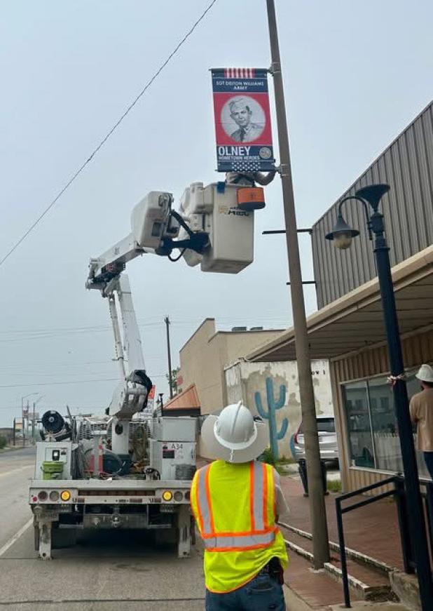Crew from Texas-New Mexico Power and Brazos Communications hung new banners created by Keep Olney Beautiful to honor the City’s military veterans along Main Street. Photo by Kyle Turner