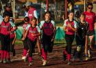 The Olney Young Guns race back to the dugout after a quick meeting at the plate; after grabbing gloves and equipment the girls excitedly take the field to begin warming up for their playoff softball game. Photo by Will Sadler
